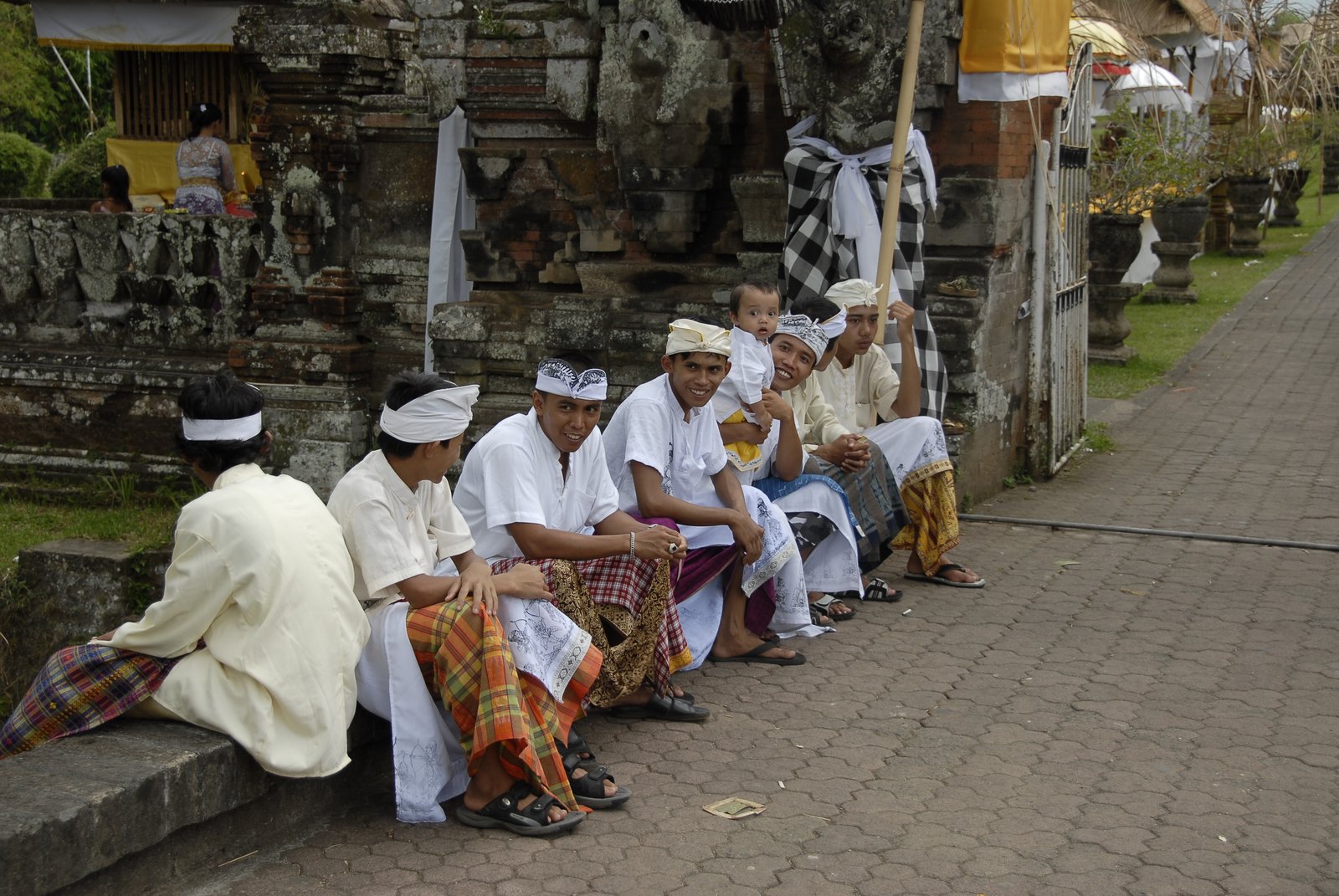 Balinese men in traditional white ceremonial dress seated outside a temple