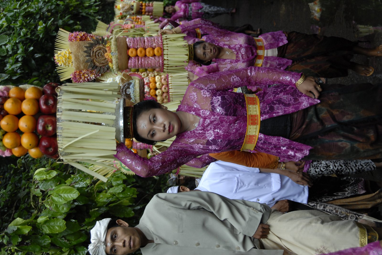Balinese woman in traditional purple ceremonial dress carrying temple offerings on her head