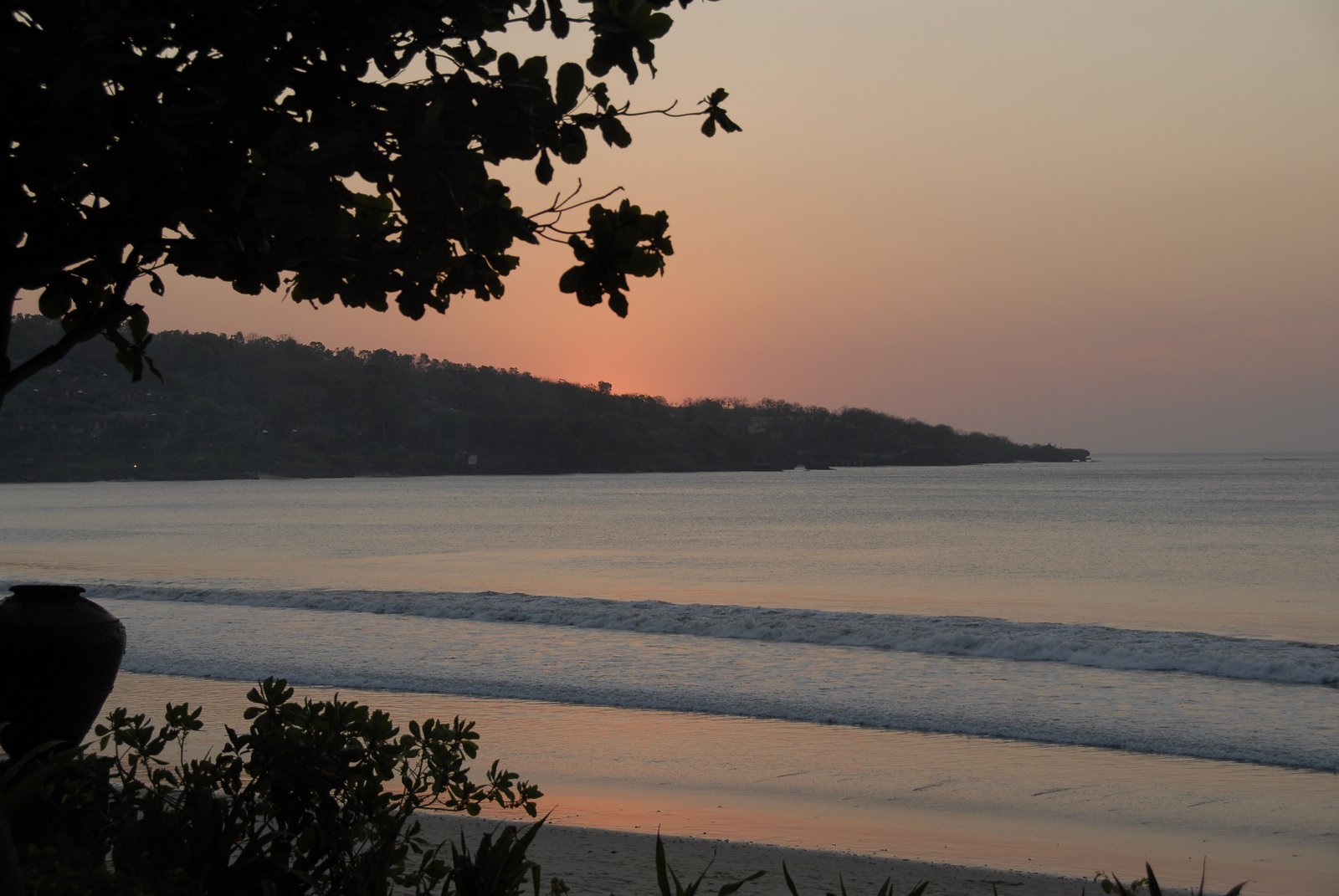 Bali coastline sunset with tree silhouettes and gentle surf