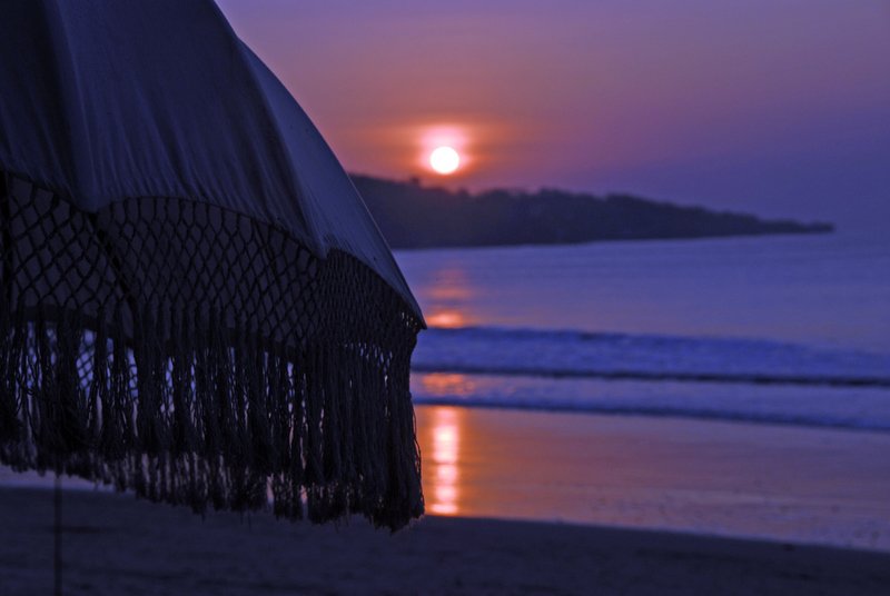 Sunset over ocean with beach umbrella silhouette, Jimbaran Bay, Bali
